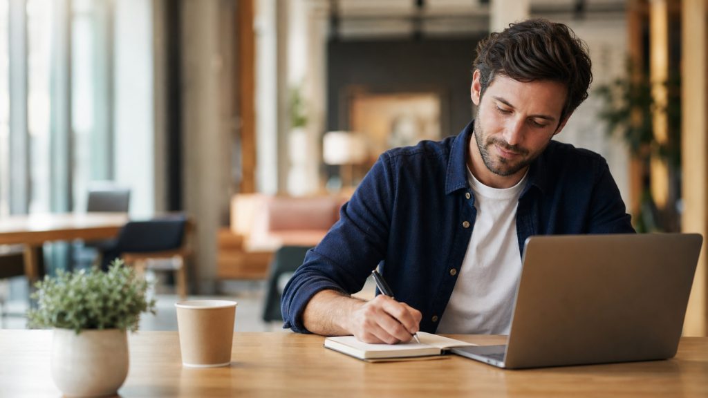 Consultant commercial écrivant une note à côté de son ordinateur dans un espace de travail lumineux, illustrant une routine de social selling LinkedIn fondée sur la relation et sans spam.